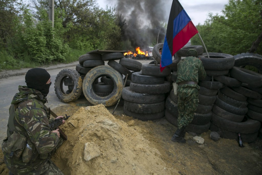 Pro-Russian separatists guard a checkpoint as tyres burn in front of them, near the town of Slaviansk